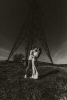 élégant modèle couple dans le montagnes dans été. une Jeune garçon et fille dans une blanc soie robe sont permanent près grand les structures de Puissance lignes. noir et blanc contraste photo