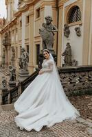 une charmant la mariée dans une magnifique robe, une longue voile, contre le Contexte de le ancien architecture de une moderne ville. une mariage couple dans le ville centre sur le escaliers. photo