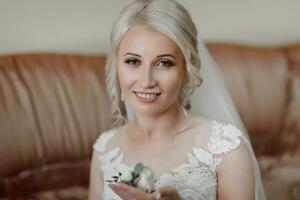 magnifique blond la mariée portrait, en portant lacet dans main mariage maquillage coiffure, magnifique Jeune femme dans blanc robe à maison. séries photo