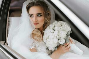 aux cheveux blancs la mariée bijoux tête séance dans une noir voiture sur votre mariage journée avec une bouquet. portrait de le la mariée. luxuriant blanc dentelle robe photo