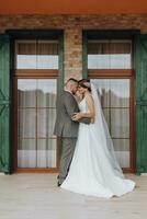 le la mariée et jeune marié sont permanent contre le Contexte de vert les fenêtres. élégant la mariée et jeune marié. mariage photo. facile atmosphère photo