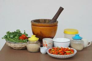 en bois mortier pilon, légumes, assiette de rouge piments, verre pot de sucre, céramique boules et tasses. concept, préparation nourriture ingrédient et équipement pour cuisson. thaïlandais traditionnel cuisine style. photo