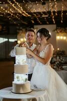 les jeunes mariés coupent et goûtent joyeusement le gâteau de mariage photo