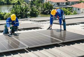 Hommes techniciens porter photovoltaïque solaire modules sur le usine toit. ingénieurs dans casques installation solaire panneau systèmes en plein air. concept de alternative et renouvelable énergie. photo