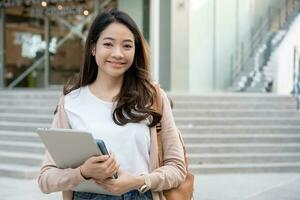 magnifique étudiant asiatique femme avec sac à dos et tablette Extérieur. sourire fille content porter une lot de livre dans Université Campus. portrait femelle sur international Asie université. éducation, étude, école photo