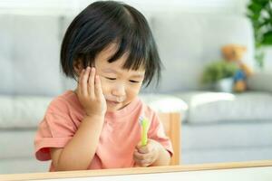 peu asiatique fille presses main à joue, souffre de douleur dans dent. les dents carie, dentaire problèmes, enfant émotions et faciale expression, oral santé se soucier, réduire bonbons, fluor enrobage photo