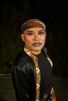 une Masculin Danseur portant une noir costume plein de batik motifs avec maquillage sur le sien visage photo