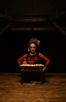 un asiatique femme dans une rouge du danseur robe est séance à une rituel offre table plein de fleurs photo