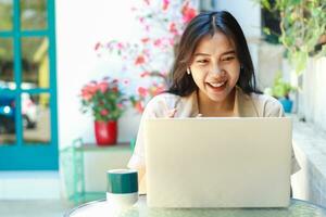 excité asiatique femme séance dans café en utilisant portable à avoir en ligne réunion portant décontractée à la mode vêtements, femelle étudiant faire présentation dans en plein air travail espace photo