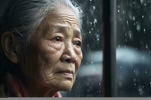 ai généré Sénior Asie femme triste et déprimé à la recherche en dehors de le fenêtre avec gouttes de pluie sur le verre fenêtre sur une pluvieux journée ,génératif ai. photo