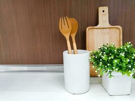 en bois ustensiles de cuisine et décorer petit vert plante dans blanc céramique vase sur cuisine étagères et en bois mur Contexte. photo