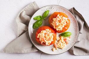 proche en haut de cuit tomate moitiés rempli avec brouillé Oeuf et basilic sur une assiette Haut vue photo