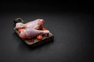brut poulet jambes avec sel, épices et herbes sur une foncé béton Contexte photo