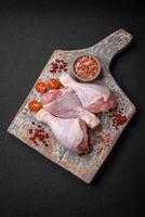 brut poulet jambes avec sel, épices et herbes sur une foncé béton Contexte photo