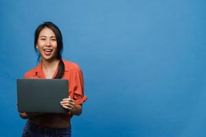 surpris une jeune femme asiatique utilisant un ordinateur portable avec une expression positive, un large sourire, vêtue de vêtements décontractés et regardant la caméra sur fond bleu. heureuse adorable femme heureuse se réjouit du succès.