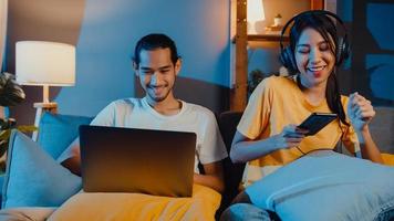 couple d'asie indépendant homme et femme dans un travail décontracté sur un ordinateur portable la nuit profitez d'une détente heureuse avec une femme portez un casque écoutez de la musique sur un smartphone chantez danse sur un canapé à la maison, vie conjugale. photo