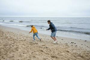 une père avec le sien fils jouer sur le l'automne plage. cool l'automne temps. photo