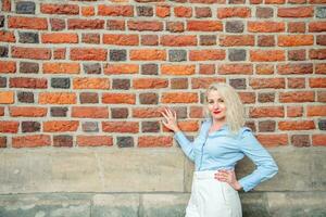 une femme d'affaires des stands contre une rouge brique mur sur le rue. une femme habillé dans blanc pantalon et une bleu chemise. espace pour copier. été photo