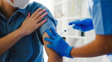 une jeune infirmière asiatique donnant un vaccin anti-virus covid-19 ou antigrippal à un patient âgé porte un masque facial contre les maladies virales à la clinique de santé ou au bureau de l'hôpital. notion de vaccination. photo