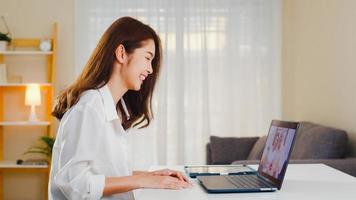 jeune femme d'affaires asiatique utilisant un appel vidéo pour ordinateur portable parlant avec le père et la mère de la famille tout en travaillant à domicile dans le salon. auto-isolement, distanciation sociale, quarantaine pour la prévention des coronavirus. photo