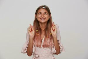 studio photo de de bonne humeur Jeune magnifique blond Dame dans de fête élégant vêtements souriant positivement et élevage mains avec franchi les doigts tandis que permanent plus de blanc Contexte