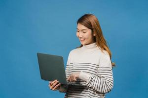 jeune femme asiatique utilisant un ordinateur portable avec une expression positive, sourit largement, vêtue de vêtements décontractés, se sentant heureuse et isolée sur fond bleu. heureuse adorable femme heureuse se réjouit du succès.