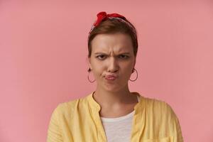 image européen marron aux cheveux jeunesse femme émotion en colère Ne pas aimer agacé ennuyé irritation à la recherche à vous posant contre rose mur portant blanc T-shirt et Jaune chemise et rouge bandana oreille anneaux photo