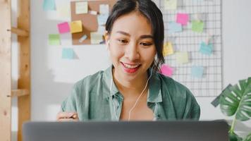 Une femme d'affaires asiatique utilisant un ordinateur portable parle à ses collègues du plan lors d'un appel vidéo tout en travaillant de manière intelligente à domicile dans le salon. auto-isolement, distanciation sociale, quarantaine pour la prévention du virus corona.