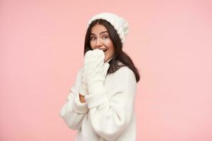 studio photo de Jeune agité brunette femelle avec Naturel maquillage élevage mains à sa bouche tandis que à la recherche joyeusement à caméra, permanent plus de rose Contexte