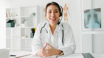 jeune femme médecin asiatique en uniforme médical blanc avec stéthoscope à l'aide d'un ordinateur portable parler vidéoconférence avec le patient, regardant la caméra dans un hôpital de santé. concept de conseil et de thérapie.