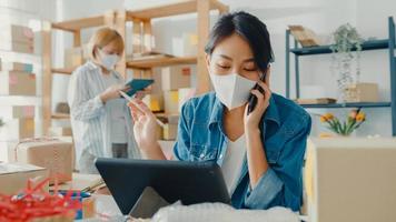 les jeunes femmes d'affaires asiatiques portent un masque facial à l'aide d'un appel téléphonique recevant la commande d'achat et vérifient le produit en stock au bureau à domicile. propriétaire de petite entreprise, concept indépendant de livraison de marché en ligne.