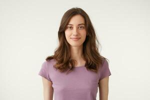 sympathique agréable magnifique foncé cheveux Jeune fille en toute confiance amical agréablement à la recherche caméra, porte violet t-shirt, isolé sur une blanc Contexte dans studio. photo