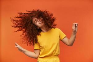 portrait de attractif, positif roux fille avec frisé cheveux. portant Jaune T-shirt. gens et émotion concept. Danse comme non un en train de regarder. supporter isolé plus de Orange Contexte photo