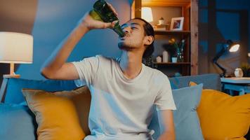 heureux jeune homme asiatique regardant la caméra profiter d'une soirée en ligne avec des amis, boire de la bière par appel vidéo en ligne dans le salon à la maison, rester à la maison en quarantaine, concept de distanciation sociale. photo