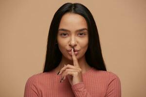 charmant Jeune femme, garde indice doigt plus de bouche, démontre Chut geste, habillé dans décontractée rose corail longtemps partir, isolé plus de blanc Contexte. ne le fais pas dire à propos mon intention. photo