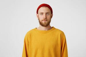 attrayant Jeune homme dans studio à la recherche à caméra.calm intéressant barbu branché gars dans rouge chapeau avec Ordinaire visage expression, fini blanc Contexte. homme prend photo pour passeport à local studio