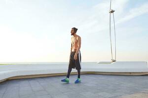 portrait de Jeune sportif homme avec barbe, du repos après jogging, des promenades à le bord de mer, Ecoutez préféré chanson sur écouteurs. jouit grands Matin photo