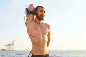 photo de Jeune Beau sportif homme avec barbe. prendre plaisir le Matin , Est-ce que élongation des exercices, a musclé corps forme, Ecoutez préféré la musique sur écouteurs.