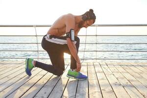 photo de Jeune Beau sportif homme avec barbe, Ecoutez préféré mélanger sur écouteurs. attacher les lacets avant jogging.