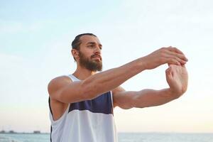 portrait de Jeune sportif barbu homme Faire une Matin yoga à le bord de mer, pistes en bonne santé actif mode de vie, regards loin. aptitude Masculin modèle. photo