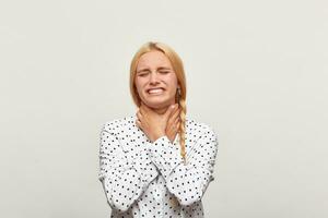 studio portrait de une blond Jeune fille avec cheveux recueillies dans tresser frustré affligé bouleversé, mains étrangler se presque pleurs. plus de blanc Contexte photo