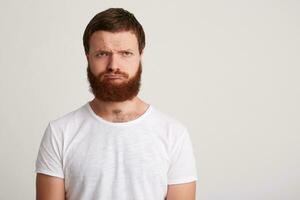 portrait de triste dérangé Jeune homme branché avec barbe porte t chemise se sent mécontent et déprimé isolé plus de blanc Contexte en pensant à propos le sien problèmes photo