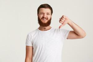 portrait de malheureux mécontent Jeune homme branché avec barbe porte t chemise se sent déçu et spectacles les pouces vers le bas geste isolé plus de blanc Contexte photo