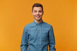 attrayant gentil mignonne Jeune homme doucement souriant habillé dans une magnifique denim chemise isolé sur une Jaune Contexte. gars parlant à le fille il aime. photo