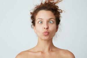 horizontal coup de incroyable fou Jeune femme avec frisé cheveux et parfait peau fabrication marrant visage et plaisanterie isolé plus de blanc Contexte joyeux fille ayant amusement après prise douche photo