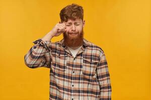 intérieur portrait de Jeune barbu Masculin avec rouge cheveux, porte décontractée chemise, pleurs et se sent très triste. isolé plus de Jaune Contexte. photo