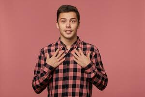 Jeune attrayant demandé homme porte dans à carreaux chemise, regards à le caméra avec content expression, point à lui-même, isolé plus de rose Contexte. photo