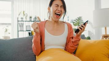 une belle dame asiatique assise sur un canapé se sent excitante avec de bonnes nouvelles à la maison. entretien de réussite, réussite des diplômés, acceptation du match de rencontres, approbation du crédit de démarrage, réussite du test, acceptation du concept d'emploi par l'employeur. photo