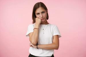 intérieur coup de bouleversé Jeune court aux cheveux Dame avec décontractée coiffure penché sa joue sur élevé main et à la recherche Malheureusement à caméra, posant plus de rose Contexte photo