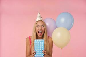 fou de joie Jeune longue aux cheveux blond Dame étant excité et surpris à avoir anniversaire cadeaux, ayant de bonne humeur des moments dans sa la vie pendant anniversaire faire la fête, posant plus de rose Contexte photo